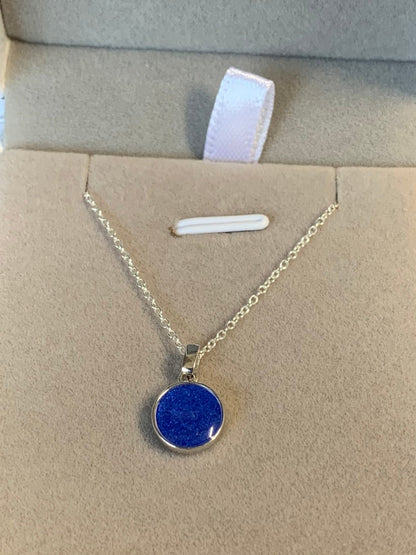 A sterling silver chain necklace with a round blue pendant made from resin with a loved ones ashes. 